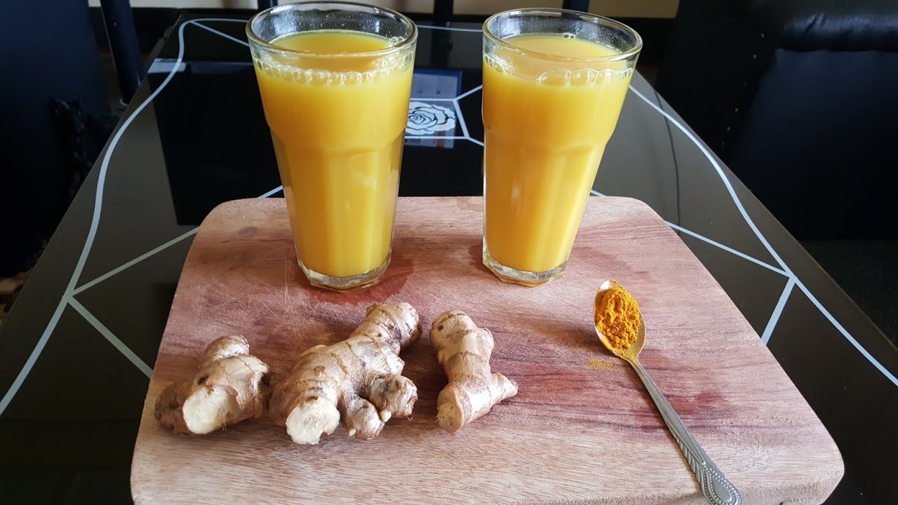 Due bicchieri con succo di zenzero e curcuma accanto a radici di zenzero fresco e cucchiaio di curcuma in polvere